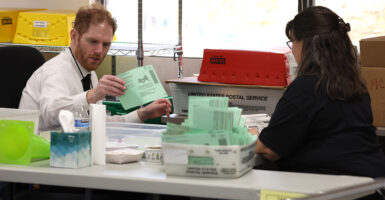 Man in a white dress shirt holds mail-in ballot as woman looks on