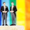 Two men in suits on a cake-topper with a rainbow flag in the background.