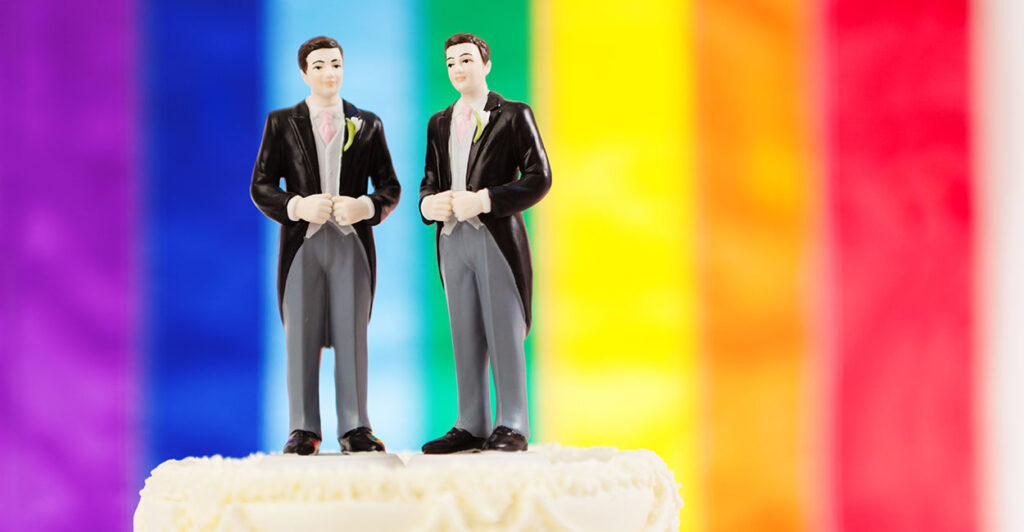 Two men in suits on a cake-topper with a rainbow flag in the background.