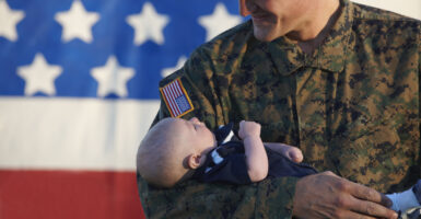 Military man holds baby in front of American flag