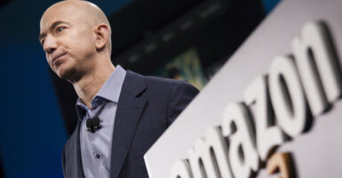 Amazon CEO Jeff Bezos in a suit near an Amazon logo.