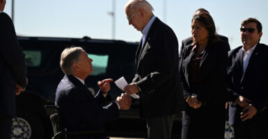 Greg Abbott hands Joe Biden a letter as both men stand in suits