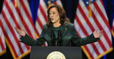 Kamala Harris gestures in a suit in front of American flags