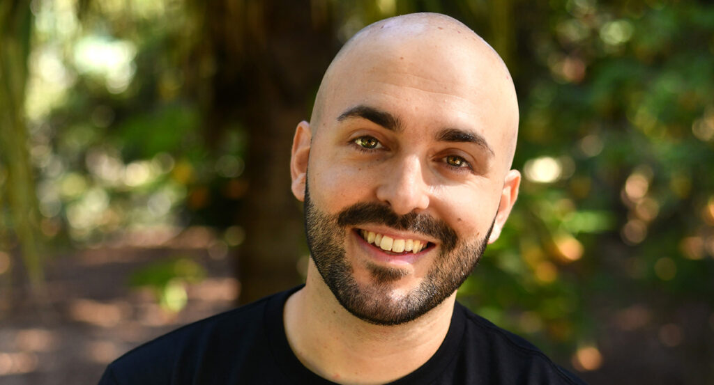Matt Grech, a bald white Maltese man with a close-cropped black beard, smiles in a forest setting