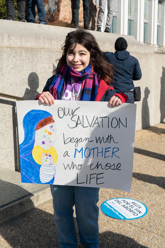 woman holds sign reading "our salvation began with a mother who chose life"