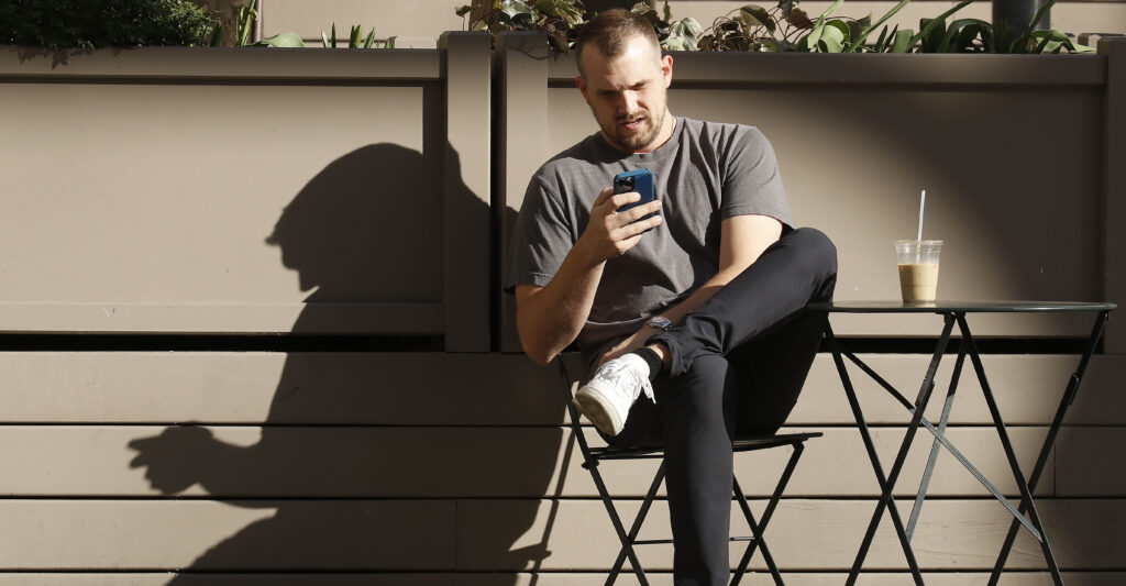 Man sitting down scrolling social media on his phone