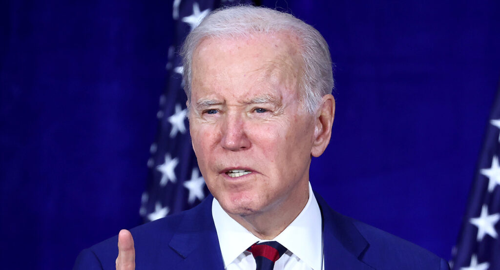 President Joe Biden in a blue suit with a blue background and American flags