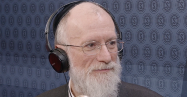 Rabbi Yaakov Menken with a white beard, glasses, and headphones in front of The Daily Signal logo