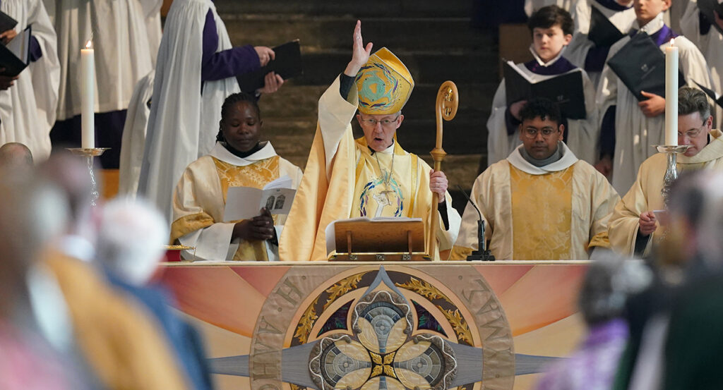 Justin Welby in gold robes makes the sign of the cross while holding a crozier at the altar of Canterbury Cathedral