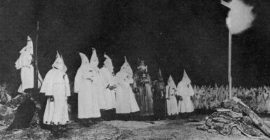 Ku Klux Klan members in white robes in front of a burning cross
