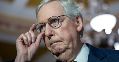 Mitch McConnell in a suit touches his glasses