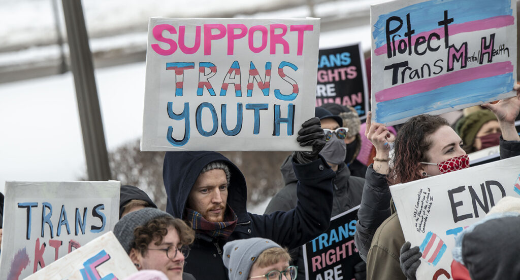 Protesters hold signs reading "support trans youth"