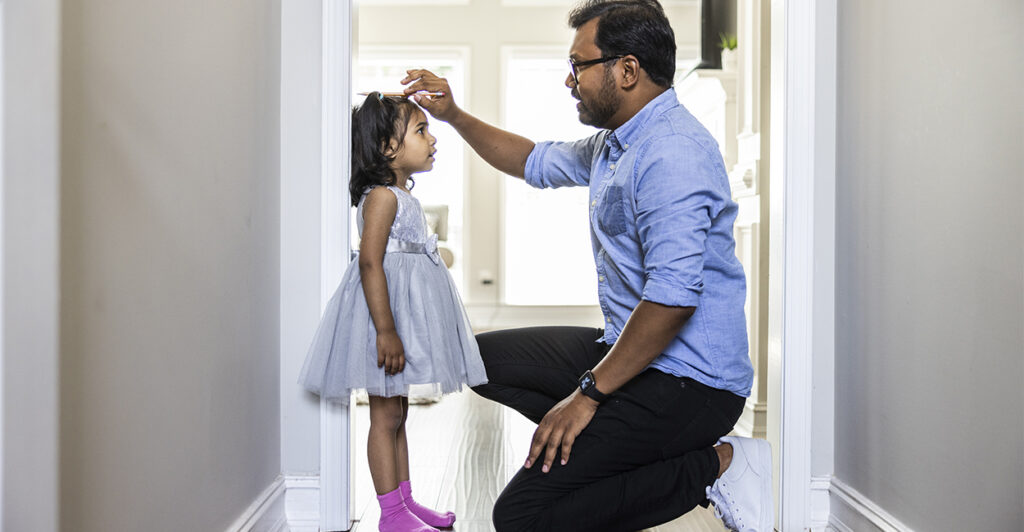 Father measuring height of 5-year-old daughter