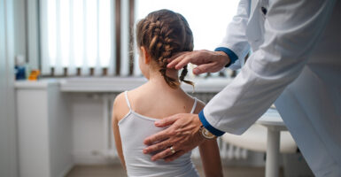 Pediatrician examining little girl, checking posture.
