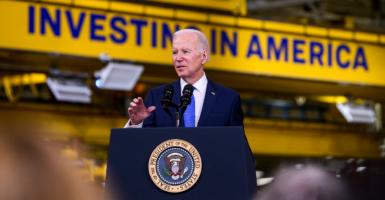 President Joe Biden in a blue suit in front of a yellow sign reading, 
