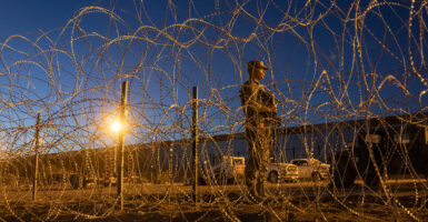 A Texas National Guard soldier stands guard behind a barbed wire fence at night at the southern border.