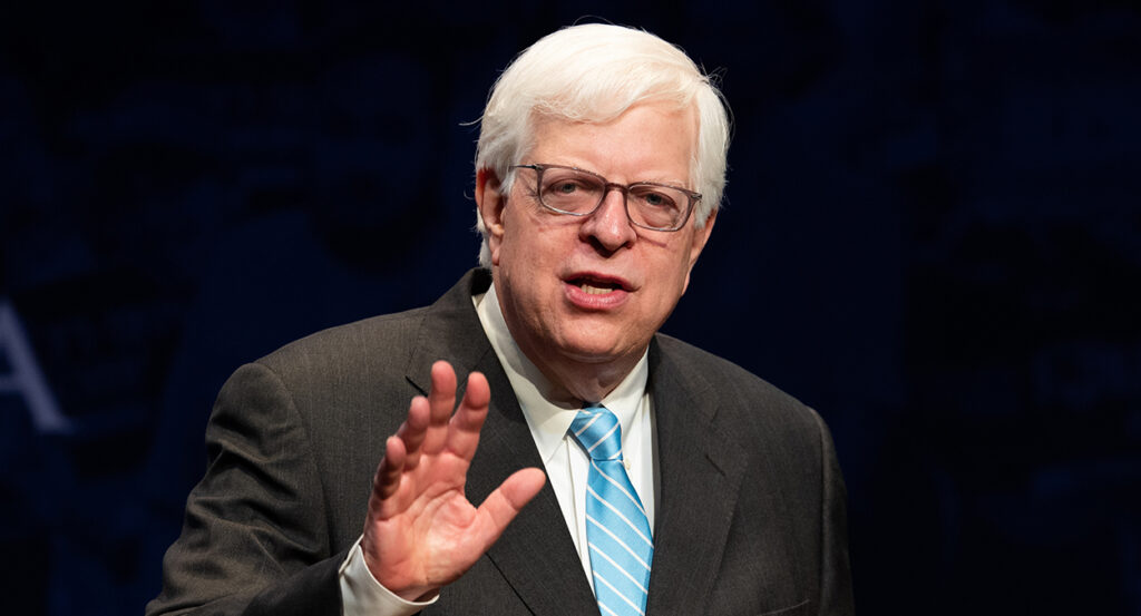 Dennis Prager speaks in a grey pin-stripe suit with a blue tie