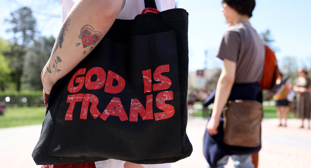 Activist holds bag reading, "God is trans"