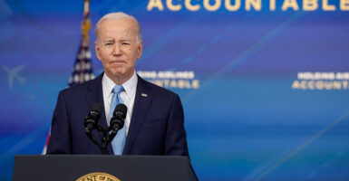 President Joe Biden speaks from stage in a dark suit and blue tie.
