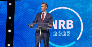 Senator Josh Hawley in a blue suit with a red tie speaks in front of the NRB 2023 logo