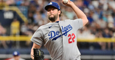 Clayton Kershaw throws a baseball while wearing a gray jersey in front of a crowd