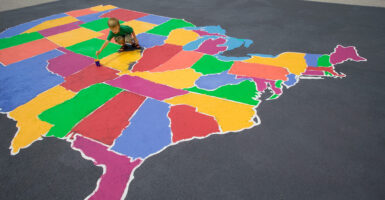 A young boy paints a large colorful U.S. map on the pavement.