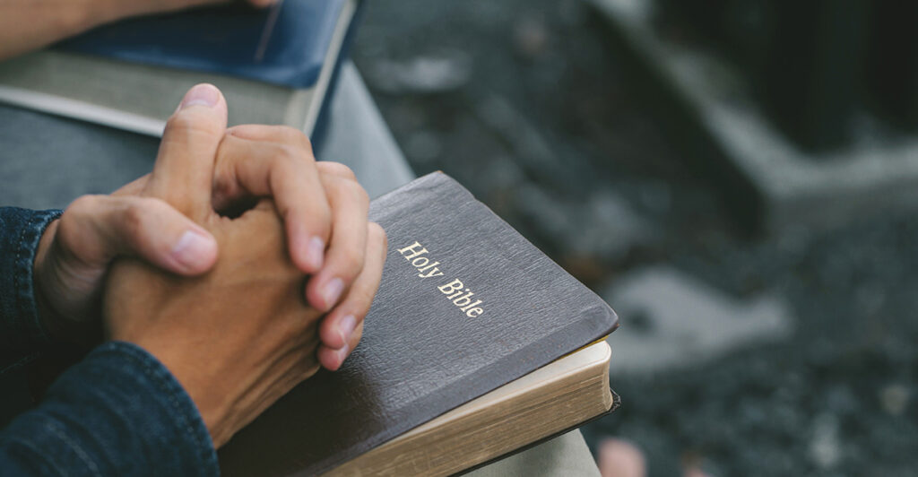 Folded hands rest on the Bible.