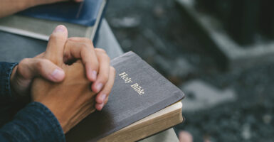 Folded hands rest on the Bible.
