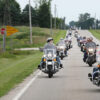 A large group of motorcyclists ride down the street.