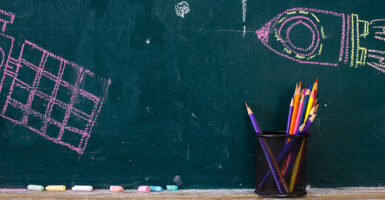 A container of colored pencils leans against a chalkboard with a small drawing of a spaceship.