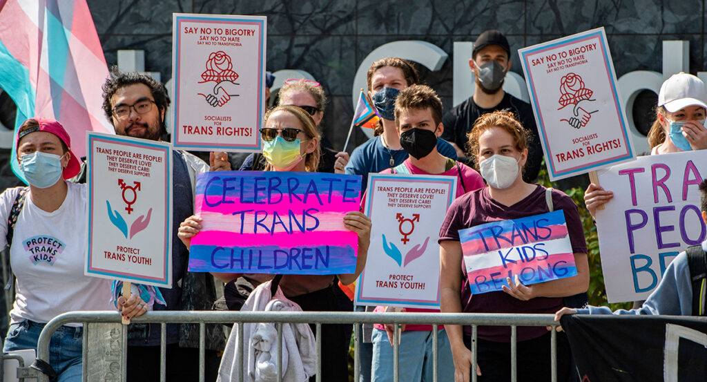 Pro-transgender activists protest with signs reading "celebrate trans children"