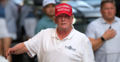 Trump walking in a white shirt and red "Make America Great Again" hat.