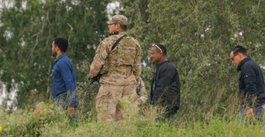 A National Guardsman escorts three male illegal aliens to Border Patrol outside.