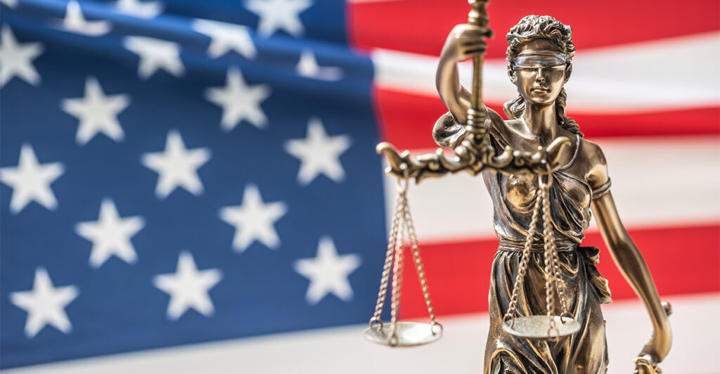 A statuette of Lady Justice in front of the American flag