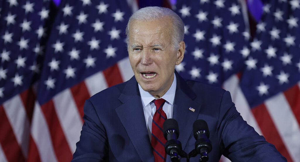 Joe Biden speaks in a blue suit in front of American flags