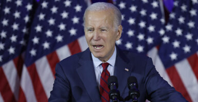 Joe Biden speaks in a blue suit in front of American flags
