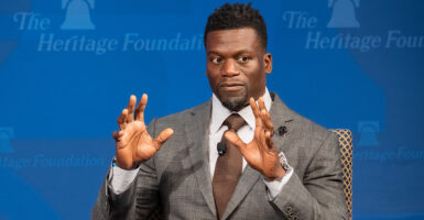 Ben Watson in a gray suit sits in front of a blue Heritage Foundation backdrop.