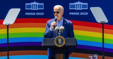 President Biden speaks in front of a pride rainbow poster.