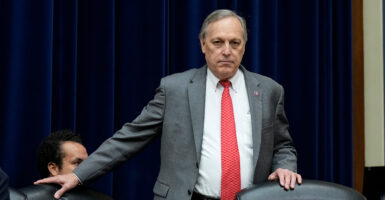 Rep. Andy Biggs, R-Ariz., prepares to take his seat at a congressional hearing wearing a grey suit, white shirt, and red tie.