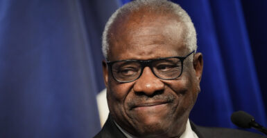 Clarence Thomas smiles in a suit in front of a blue background