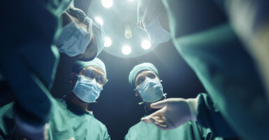 Doctors operate above a patient while wearing masks and head coverings