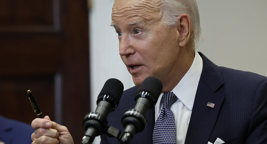 Joe Biden in a suit with a blue tie holds a pen