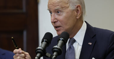 Joe Biden in a suit with a blue tie holds a pen