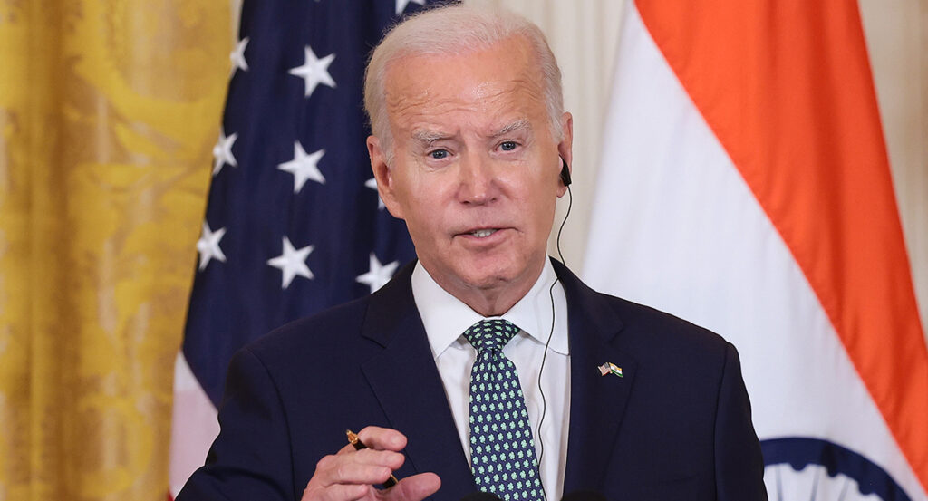 Joe Biden speaks wearing a suit in front of an American flag and an India flag