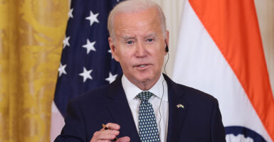 Joe Biden speaks wearing a suit in front of an American flag and an India flag