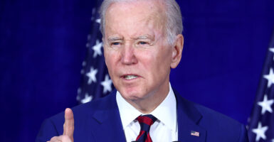 Joe Biden in a blue suit with an American flag pin raises a finger