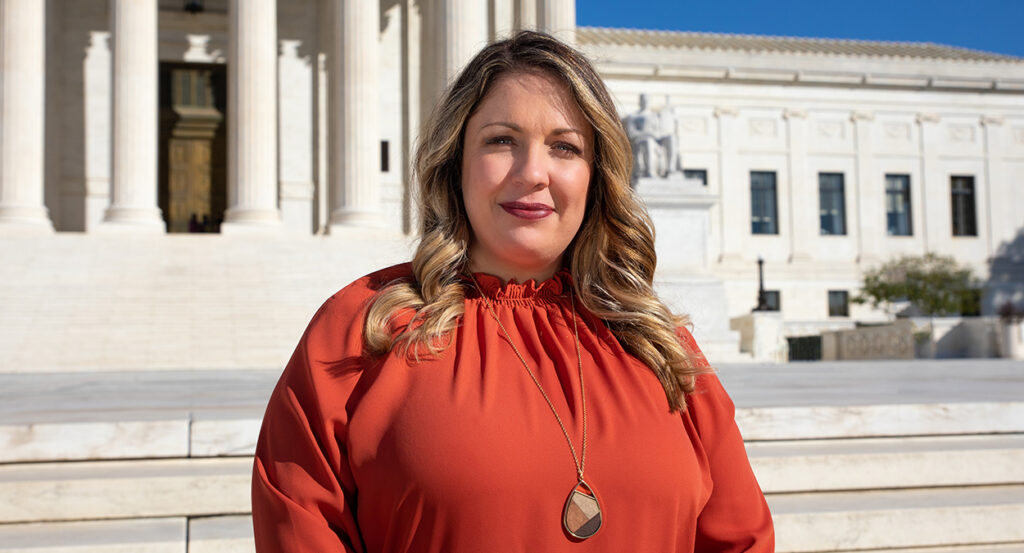 Lorie Smith in a red dress standing in front of the Supreme Court