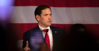 Sen. Marco Rubio, R-Fla., speaks to a crowd wearing a dark suit and red time with a large American flag behind him.