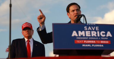Former President Donald Trump stands behind Sen. Marco Rubio, R-Fla., as Rubio speaks to a crowd from a podium bearing a sign that reads "Save America."