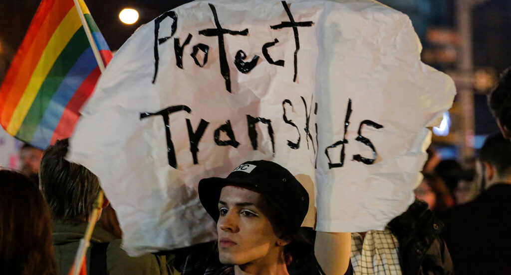 Activist marches with a sign reading "protect trans kids"